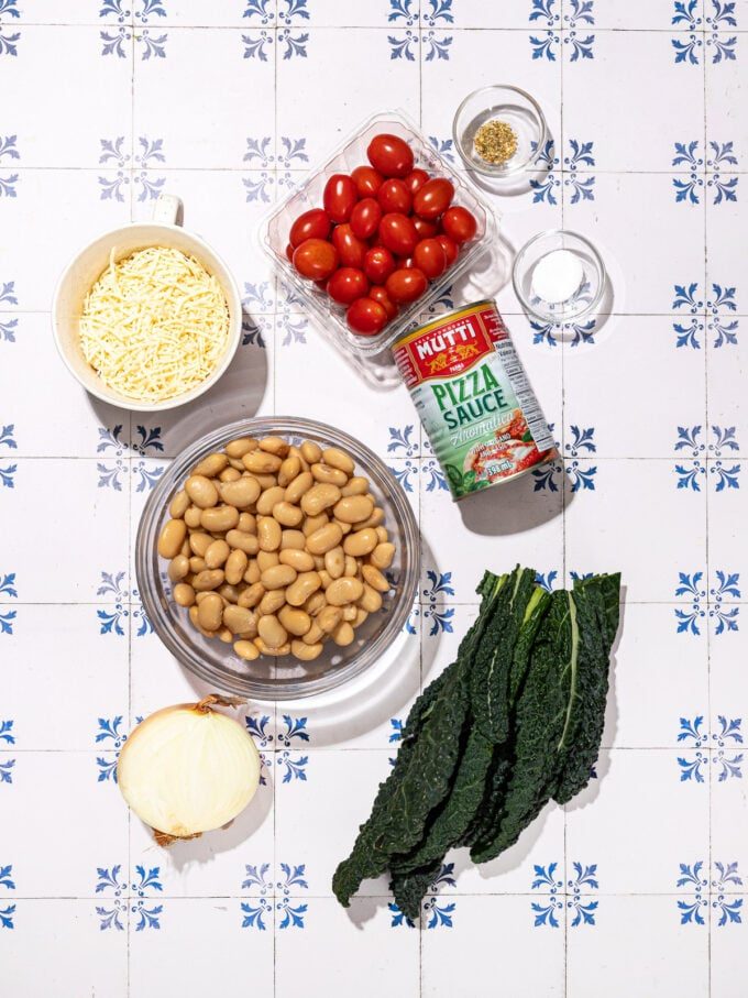 fresh kale, cherry tomatoes, onion, and bowls of butter beans, vegan cheese shreds and spices