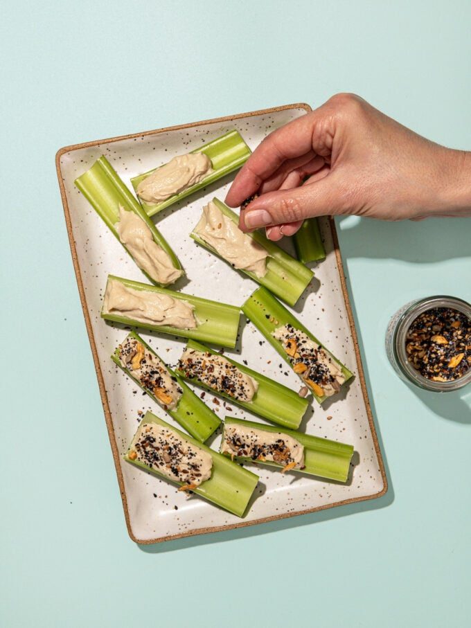 hand sprinkling everything bagel seasoning on tahini stuffed celery