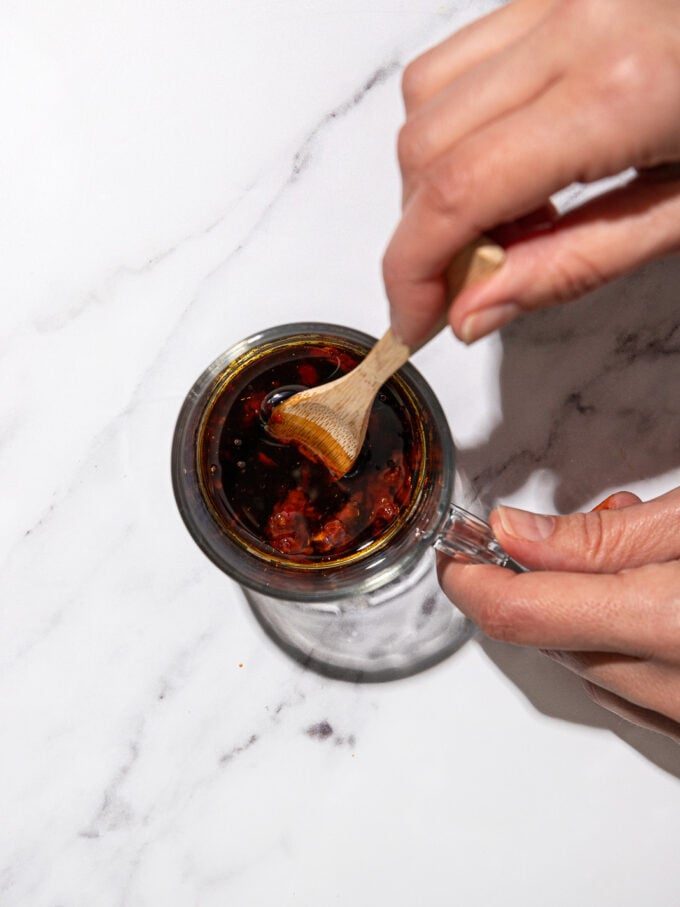 stirring soy and chili sauce with a wooden spoon in glass jar