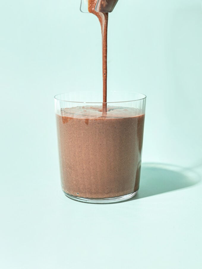 pouring black bean chocolate smoothie into a glass on a blue background