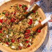 hands tossing a farro vegetable salad in a wooden bowl