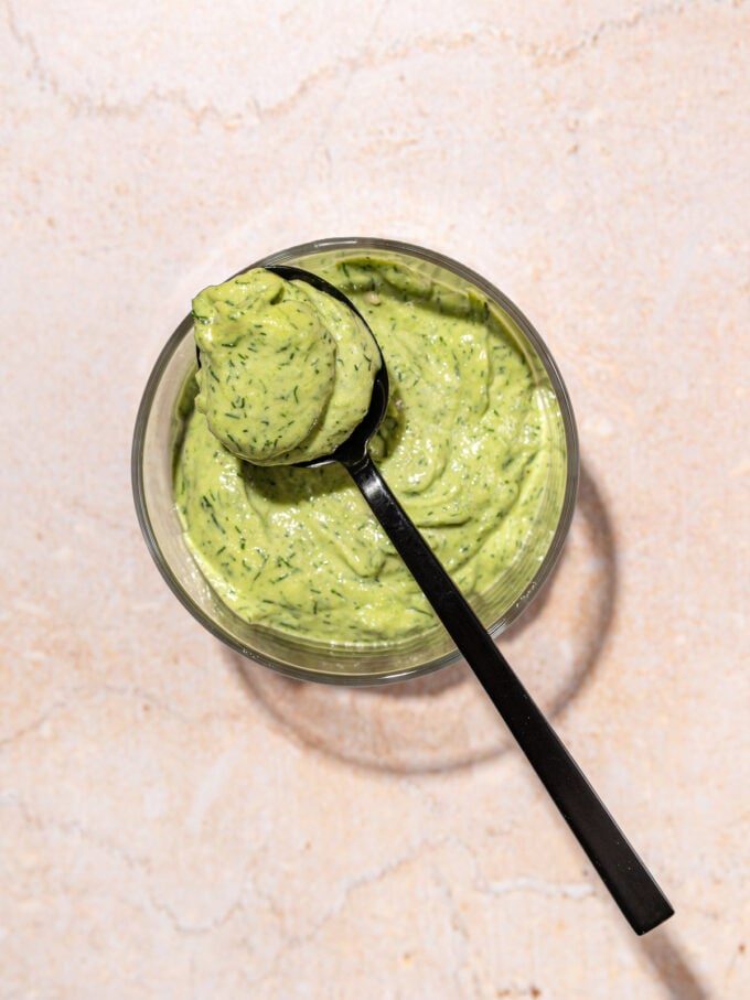 Green goddess dressing in glass bowl with black spoon resting on top