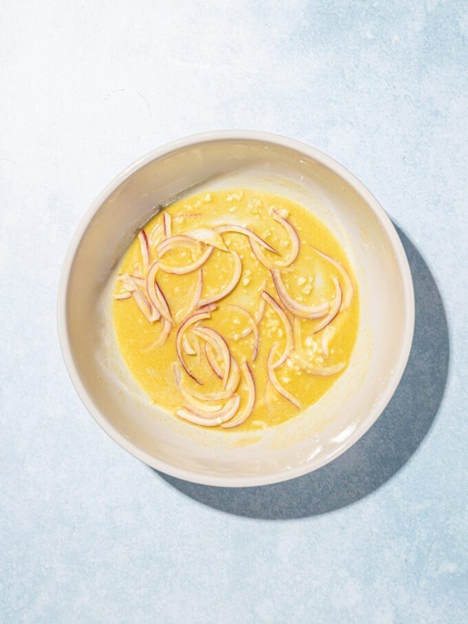 garlic and sliced onion in dressing in white bowl