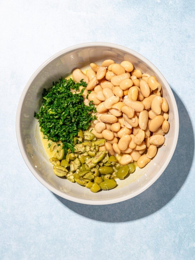 white bowl with minced parsley, butter beans and olives inside