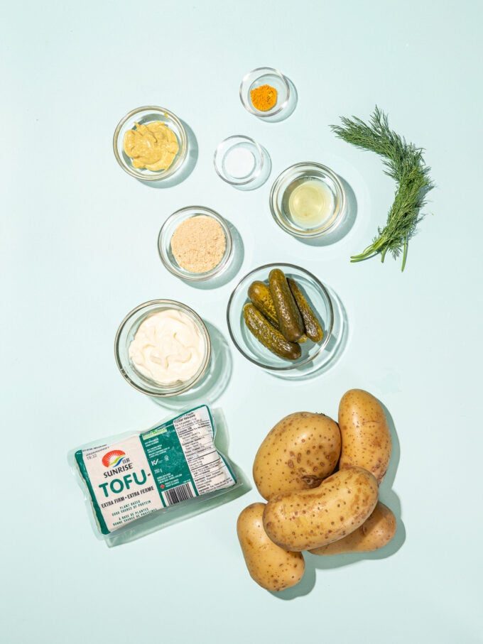 yukon gold potatoes with a package of tofu and small bowls of potato salad ingredients: dill pickles, nutritional yeast, mayo