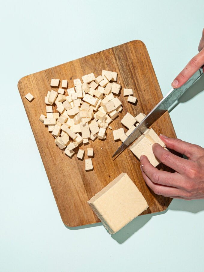 hand dicing tofu with knife on wooden cutting board