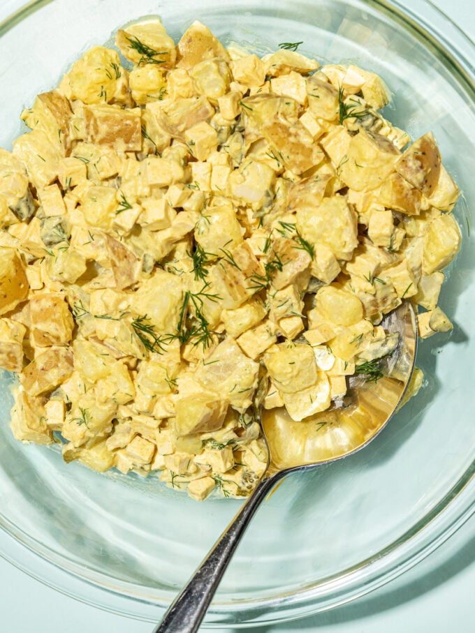 glass bowl of creamy vegan potato salad with a spoon inserted