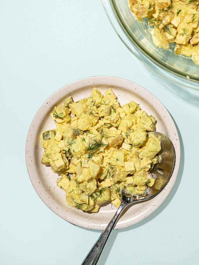 white plate topped with vegan potato salad, with a spoon.