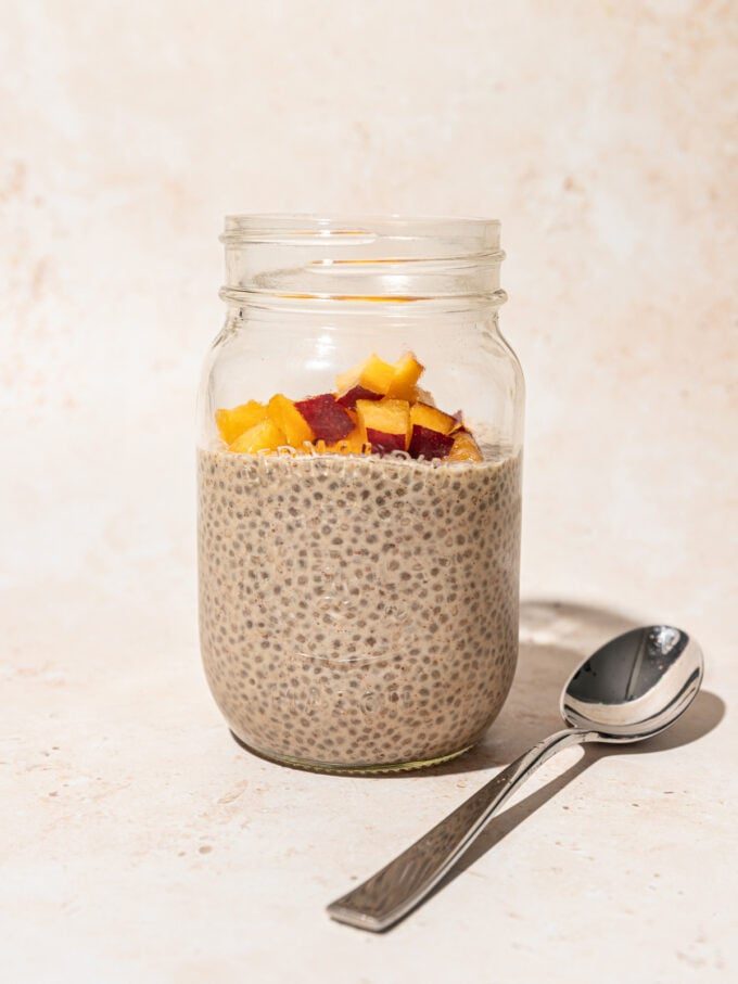 mason jar filled with chia seed pudding, topped with diced peach, with a spoon lying beside the jar
